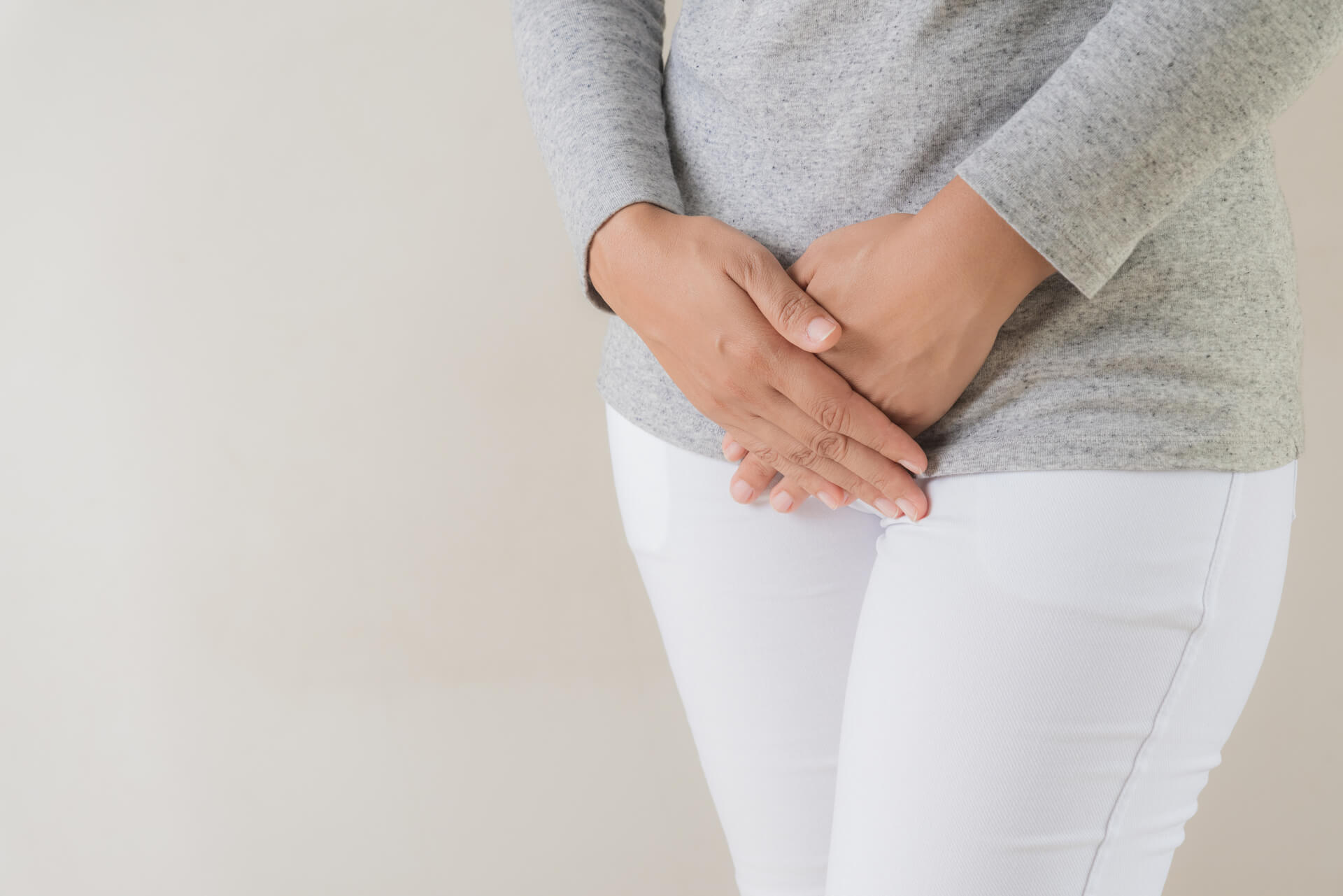 Woman holding her pelvic area with both hands, indicating discomfort.