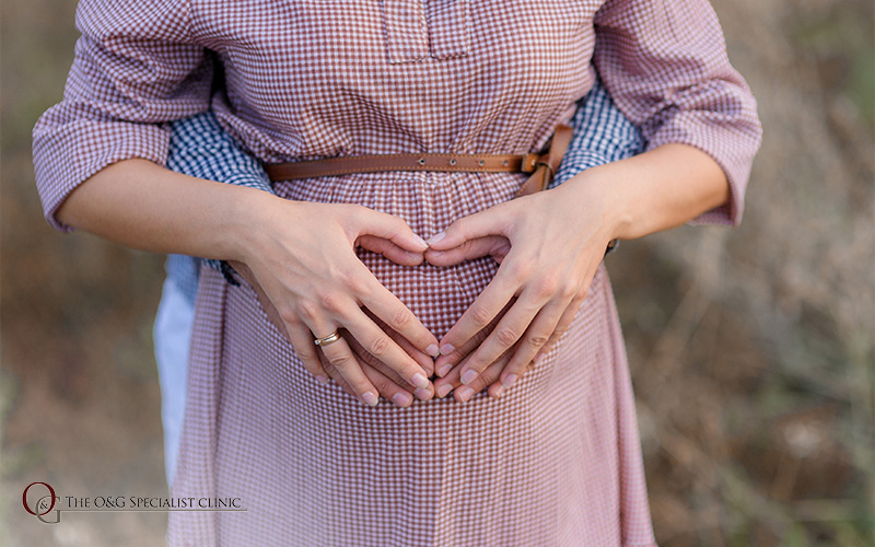 Couple's hands forming a heart on pregnant belly.