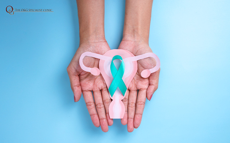 Hands holding a teal ribbon and paper uterus for cervical health.