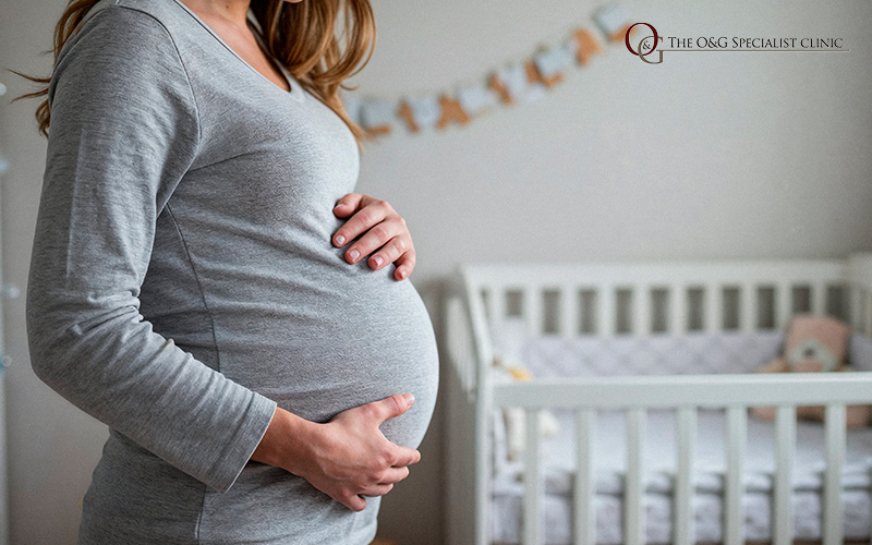 Pregnant woman holding belly next to baby crib.