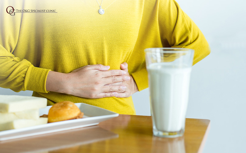 Woman holding stomach, with food and milk, experiencing bloating.